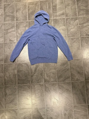 Blå hoodie med huva och snörning - Snygg blå hoodie med huva och snörning framtill. Tröjan har långärmade ärmar och en klassisk passform. Perfekt för dig som gillar en enkel och stilren look. Materialet känns mjukt och skönt mot huden.