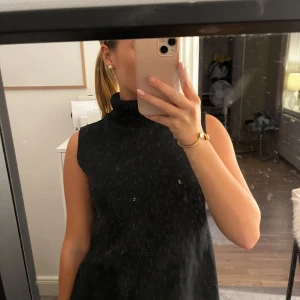 Svart stickad ärmlös klänning Zara - Svart stickad klänning från Zara med hög polokrage och ärmlös design. Klänningen har en ribbad struktur upptill och är i en kortare modell som ger en clean och stilren look. Perfekt för dig som gillar minimalistisk stil och vill ha något enkelt men snyggt.