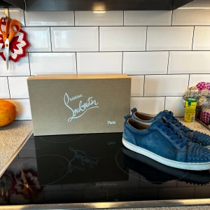 Louboutin med spikar - Snygga blå sneakers från Christian Louboutin i mocka med coola nitar på tån. Skorna har rund tå, snörning och vit platt sula. Perfekta för dig som vill sticka ut med exklusiv streetstyle. Kommer med originalkartong och dustbags.
