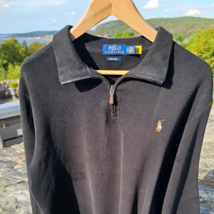 Svart Polo half zip - Svart långärmad pikétröja från Polo Ralph Lauren med klassisk krage och half zip-dragkedja. Broderad logga på bröstet och mjukt bomullsmaterial.