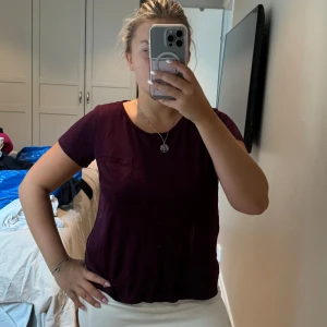 Mörklila t-shirt från H&M Divided - En enkel och snygg mörklila t-shirt från H&M Divided, modell Basic. Toppen har rund hals, korta ärmar och en liten bröstficka på vänster sida. Perfekt att matcha med jeans eller kjol för en chill look.