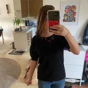 Svart blus med puffärm - Säljer en svart blus med korta puffärmar och rund hals. Tyget har en lätt struktur som ger en snygg känsla och blusen har en normal passform. Perfekt att styla med jeans eller kjol för en clean look.