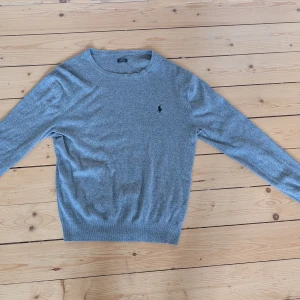 Grå slim fit tröja från Polo Ralph Lauren - Snygg grå långärmad tröja från Polo Ralph Lauren i slim fit-modell. Tillverkad i mjuk pima bomull och har den klassiska broderade loggan på bröstet. Perfekt för dig som gillar stilrena och bekväma plagg.