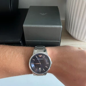Emporio Armani silverklocka - Säljer min klocka från Emporio Armani med mörkblå urtavla och datumvisning. Säljer på grund av att den aldrig har kommit till användning.
