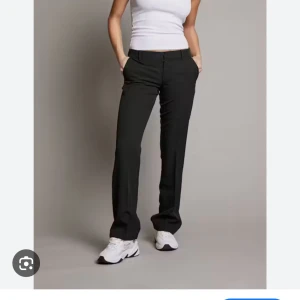 Svarta kostymbyxor med slits längst ner - Snygga svarta kostymbyxor med raka ben och klassisk passform. Byxorna har midja med hällor, diskret dragkedja och knapp framtill. Perfekta till sneakers eller boots för en clean look.