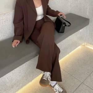 Bruna vida kostymbyxor - Mörkbruna kostymbyxor med hög midja och vida ben. Snygg klassisk look med pressveck och diskreta fickor bak. Perfekta att styla med sneakers eller boots för en trendig vibe.