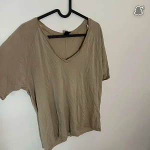 Beige v-ringad t-shirt från Lindex - En enkel och chill beige t-shirt från Lindex med v-ringad hals. Modellen är kortärmad och har en loose fit som gör den skön att bära. Materialet är mjuk bomull och färgen är neutral, perfekt till jeans eller shorts.