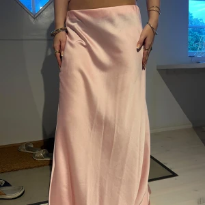 Ljusrosa långkjol i satin - Supersnygg ljusrosa långkjol i satin. Kjolen har en enkel och rak siluett som faller snyggt längs benen. Perfekt för dig som vill ha en feminin och trendig look.🩷