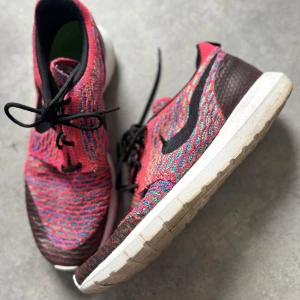 Nike sneakers i färgglad mix - Nike Flyknit sneakers med färgglad ovandel i rött, blått och grönt. Skorna har svart swoosh, svarta skosnören och vit sula. Ovandelen är stickad för en lätt och luftig känsla. Perfekta för dig som gillar unika och sportiga sneakers.