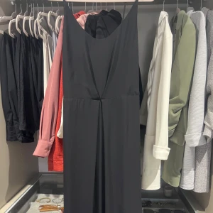 Svart långklänning med djup rygg - Snygg svart långklänning med djup v-ringad rygg och mjukt fallande tyg. Klänningen är ärmlös och har en elegant drapering framtill. Perfekt som festklänning! Storlek S/XS