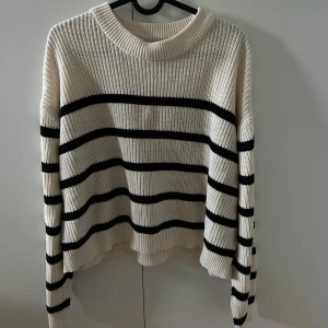 Randig stickad tröja från H&M - Säljer en krämvit stickad tröja från H&M med svarta horisontella ränder. Tröjan har en bred ribbad krage och långa ärmar. Chill höst- eller vinterstil.