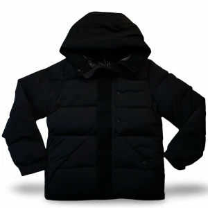 Moncler Madeira - Säljer en svart pufferjacka från Moncler med stor huva och tydlig logga på ärmen. Jackan har quiltad design, tryckknappar och dragkedja framtill. Perfekt för kalla dagar och riktigt snygg streetstil. Moncler-detaljer på bröstet och ärmen för extra premiumkänsla.
