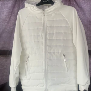 Vit cardigan jacka  - Snygg vit cardigan. Jackan har dragkedja hela vägen, två fickor med dragkedja och en skön huva. Perfekt för kyliga dagar när du vill ha en clean och stilren look.