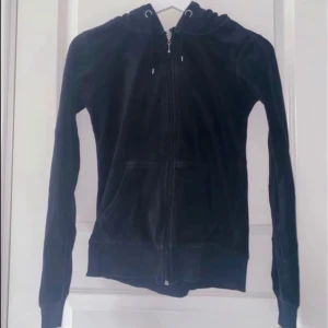 Svart velour hoodie med dragkedja - Mysig svart hoodie i mjuk velour med huva och snörning. Tröjan har hel dragkedja framtill och två fickor. Perfekt för chill dagar eller när du vill ha en skön och avslappnad stil.