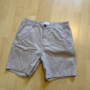 Beige shorts från Studio Total - Säljer ett par stilrena beige shorts från Studio Total. De har normal passform, elastisk midja med knapp och dragkedja samt sidofickor. Perfekta för varma dagar och enkla att matcha med det mesta.