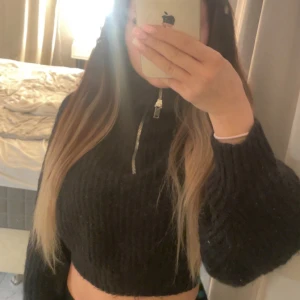 Svart croppad stickad tröja half zip - Svart croppad stickad tröja med halv dragkedja i halsen. Tröjan har långärmade, lite pösiga ärmar och ribbad struktur. Perfekt för dig som gillar en trendig och mysig look med lite edge.