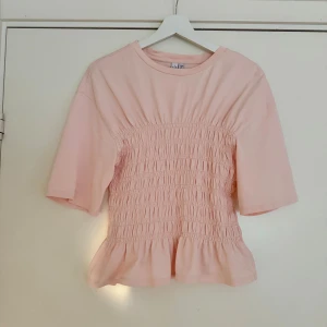 Ljusrosa blus  - Supersöt ljusrosa blus från & Other Stories med smockad midja och volangkant nedtill. Topp med rund hals, korta ärmar och mjukt bomullstyg. Sparsamt använd💞💞