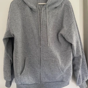 Grå hoodie med dragkedja, storlek M - Mjuk och chill grå hoodie i medium med huva, snörning och dragkedja framtill. Har två stora fickor och ribbade muddar vid ärmar och nederkant🩶🩶🩶🩶
