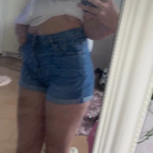 Blå högmidjade jeansshorts Lindex - Snygga blå jeansshorts från Lindex med hög midja och klassisk femficksdesign. Modellen är tight och har uppvikta benslut för en fräsch look. Perfekta för varma dagar och passar till allt. Materialet är slitstarkt denim och färgen är klassiskt blå. Lite stretchiga så vid ålder 12-14 kan man ha på sig