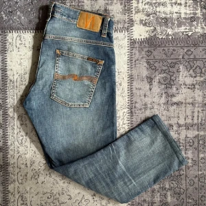 Blå Nudie Jeans - Snygga blå jeans från Nudie. Modellen är grimtrim. Köpte på Plick men är för små för mig. 32/30 men uppsydda och därför kortare. Längd 89cm. Hör av dig om du har frågor:)