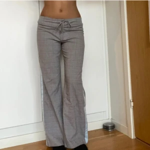 Grå rutiga byxor med snörning - Snygga grå byxor med diskret rutigt mönster och snörning i midjan. Modellen har bootcut-ben och låg midja, vilket ger en avslappnad men trendig vibe. Skriv för frågor 🥰helt nya 