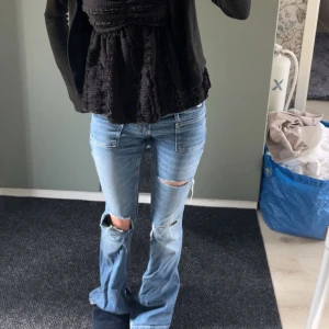 Lågmidjade bootcut jeans med slitningar - Säljer ett par ljusblå jeans med låg midja och bootcut-ben. Jeansen har slitna detaljer och hål vid knäna. Hålet på ena knät spräckte och är nu sytt