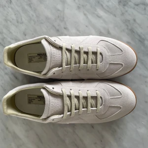 Maison Margiela Gats  - Tja! Säljer dessa feta Maison Margiela Gats i en ljusbeige mocka med klassisk gummisula. Snygg minimalistisk design med rund tå och ton-i-ton snörning. Perfekta för dig som gillar stilrena och exklusiva sneakers med premiumkänsla. Hör av er vid frågor eller funderingar!
