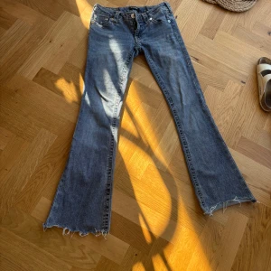 True Religion bootcut jeans blå - Säljer ett par blå jeans från True Religion med bootcut passform och råa, fransiga benslut. Klassiska bakfickor, dom är avklippta och insydda i midjan för att bli lite mindre storlek w24 men passar w23
