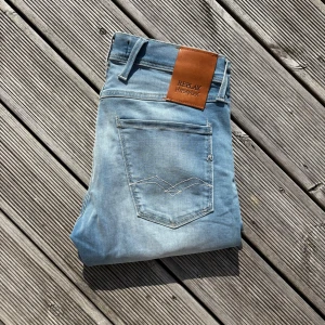 Replay Anbass ljusblå jeans - Säljer ett par Replay Anbass Hyperflex jeans i ljusblå tvätt. De har klassisk femficksdesign, snygga slitningar och en skön stretchig känsla. Märkespatch i läder baktill och Replay-logga på myntfickan. Perfekta för dig som gillar en modern och bekväm look. W27 L32