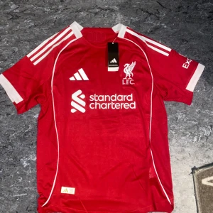 Liverpool FC röd matchtröja Adidas S - Liverpool FCs officiella röd matchtröja från Adidas med vita detaljer och tryck. Kortärmad med klassiska tre ränder på axlarna, klubbmärke på bröstet och spelarnamn Wirtz samt nummer 7 på ryggen.Den är  oanvänd, ny pris 1950.