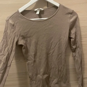 Beige ribbad långärmad topp H&M - En basic beige långärmad topp från H&M med rund halsringning och ribbad struktur. 