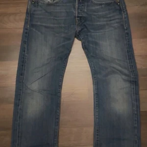Blå Replay jeans straight fit - Snygga blå Replay jeans med klassisk tvätt och raka ben. Jeansen har fem fickor, tydliga slitningar och Replay-logga på fickan samt läderpatch bak. Tillverkade i robust denim som ger en cool och avslappnad look. Storlek 28/32