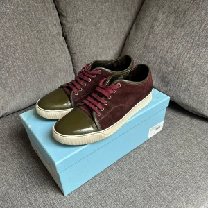 Lanvin sneakers i vinröd mocka - Snygga sneakers från Lanvin i vinröd mocka med olivgröna detaljer och tå i lack. Skorna har vita sulor och matchande vinröda skosnören. Knappt tecken på användning finns inga synliga defekter osv uk 8 sällsynt färg då dom inte tillverkas längre skriv vid minsta fundering!