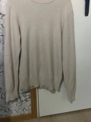 Beige stickad tröja från J.Lindeberg - Säljer en beige stickad tröja från J.Lindeberg i storlek M. Tröjan har rund hals, ribbade muddar och är långärmad. Perfekt för lager-på-lager under hösten och vintern. Enkel och stilren design som funkar till många olika outfits.