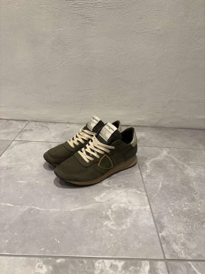 Philippe model trainers - Snygga gröna Philippe Model trainers med beige detaljer och snörning. Skorna har en rund tå, platt sula och är tillverkade i mocka med en cool gul kant runt loggan på sidan. Perfekta för dig som gillar stilrena och trendiga sneakers. Skorna kommer med låda och dustbag. Storleken är i 41