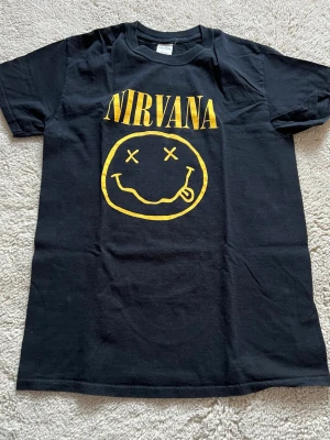 Svart Nirvana t-shirt  - Svart t-shirt från Gildan med klassiskt Nirvana-tryck i gult framtill. T-shirten har rund hals, korta ärmar och är gjord i kraftig bomull. Tröjan har inga defekter. 