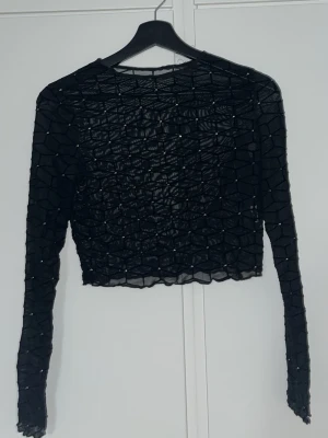 Svart mesh topp med nätmönster - Säljer en svart mesh topp med lång ärm och  nätmönster. Toppen är croppad och har transparent material. Använt några gånger på fest och är från SHEIN 