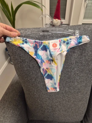Färgglad bikiniunderdel från Bik Bok - Säljer en bikiniunderdel från Bik Bok i modellen 'Even higher bottom'. Den har ett färgstarkt abstrakt mönster i blått, rosa, gult och vitt. Materialet är mjuk polyester med elastan för extra stretch. Perfekt för dig som gillar att sticka ut på stranden.