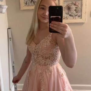 Ljusrosa långklänning med spetsdetaljer - Superfin ljusrosa långklänning med tunna axelband och v-ringning. Klänningen har vackra spetsdetaljer och blommiga broderier över hela livet och kjolen. Perfekt för bal eller student! Kjolen är lätt och faller snyggt. Nypris 8000kr!