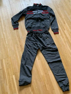 Mörkgrå mjukisbyxor från Hilfiger - Säljer ett par mörkgrå mjukisbyxor från Hilfiger med elastisk midja och dragkedjefickor. Byxorna har en broderad logga på benet och är gjorda i mjukt bomullsmaterial. Perfekt för chill dagar och sportiga aktiviteter.