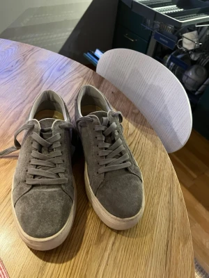 Grå mockasneakers från Vagabond - Säljer ett par grå sneakers från Vagabond i storlek 39. Skorna har en snygg mockayta, rund tå och platt sula. Klassisk snörning och diskret design som passar till jeans eller shorts. Perfekt för dig som gillar stilrena och bekväma sneakers.