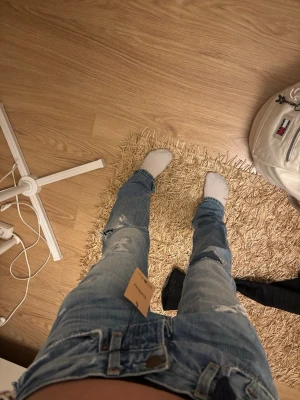 Ljusblå slitna jeans från Hollister - Säljer ett par ljusblå jeans från Hollister med snygga slitningar och hål på benen. Modellen har klassisk femficksdesign, normal passform och raka ben. Jeansen är gjorda i bomull och har en cool, lite ruffad look som passar perfekt till sneakers.