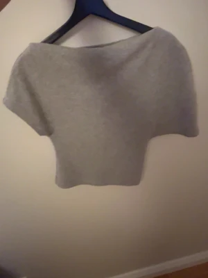 Grå croppad topp från Gina Tricot - Säljer en enkel och stilren grå croppad topp från Gina Tricot i storlek XS. Toppen har en loose passform och är tillverkad i mjuk bomull. Den är ärmlös och har en bred halsringning som ger en avslappnad vibe. Den är även snedskuren och använt denna en gång 