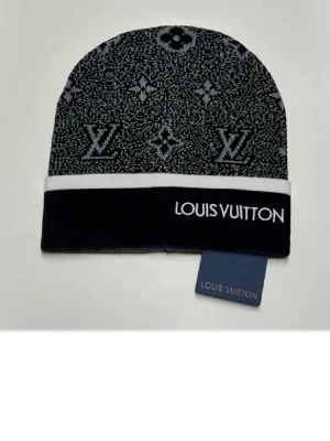 Louis Vuitton svart väst med mönster texten grå - Säljer en svart väst från Louis Vuitton med ikoniskt LV-mönster i grått och vitt. Västen har en stilren design med vit kant och logotyp framtill. Materialet känns mjukt och är troligen stickad syntet eller ull. Perfekt för dig som gillar exklusiva märken och vill sticka ut.