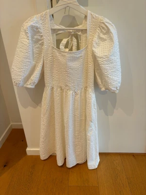 Vit omlottklänning med puffärm - Säljer en vit klänning med puffärmar och snygg struktur i tyget. Klänningen har en fyrkantig urringning och knytning i ryggen som ger en fin detalj. Perfekt till studenten eller skolavslutning!