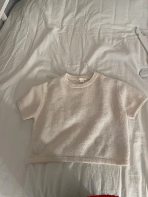Beige croppad stickad topp - Säljer en beige croppad stickad topp med korta ärmar och rund hals. Toppen har en enkel och stilren design med ribbad kant vid halsen. Perfekt att matcha med jeans eller kjol för en chill look.