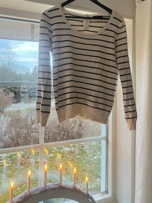 Vit och marinblå randig stickad tröja - Snygg stickad tröja i vit med marinblå ränder och rund hals. Tröjan har lång ärm och ribbade muddar vid ärmslut och nederkant. På ryggen finns fyra dekorativa knappar upptill. Jättesnygg!! Storlek L men passar mer S möjligtvis M