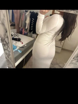 Vit långärmad långklänning - Säljer en stilren vit långklänning med lång ärm och rundad urringning. Klänningen har en tight passform och är gjord i ett mjukt, stretchigt material som sitter snyggt på kroppen. 