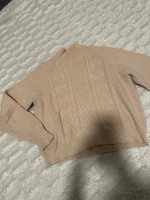 Beige stickad polotröja från Bubbleroom - Säljer en beige stickad polotröja från Bubbleroom i storlek S. Tröjan har ett snyggt kabelstickat mönster framtill och ribbade muddar vid hals, ärmslut och nederkant. Perfekt för dig som gillar mysiga och stilrena plagg med lite struktur.