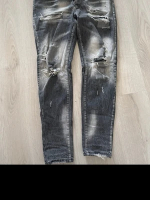 Svarta slitna jeans med hål - Säljer ett par svarta jeans med slitningar och hål på både fram- och baksida. Jeansen har en tvättad look med ljusare partier och är i en rak modell. Perfekta för dig som gillar en edgy och avslappnad stil. Skriv till mig om ni vill ha mer bilder så skickar jag mer bilder och fraktar inom 24 timmar